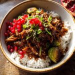 A delicious bowl of Sticky Sesame Ginger Chicken Crockpot Recipe served over rice, garnished with Brussels sprouts, pomegranate seeds, and sesame seeds.