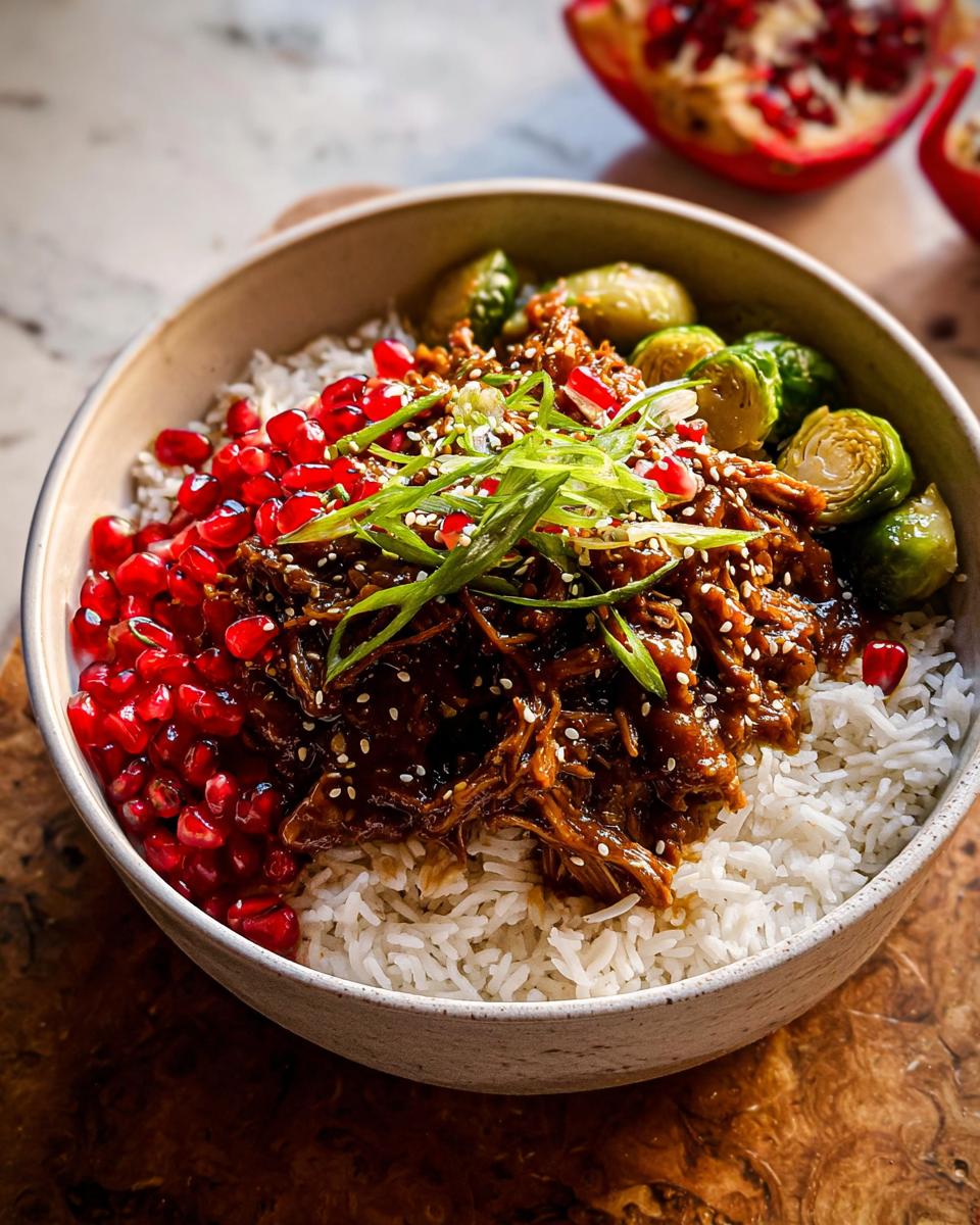 Sticky Sesame Ginger Chicken: Easy Crockpot Magic 4 A bowl of white rice topped with shredded Sticky Sesame Ginger Chicken, Brussels sprouts, and pomegranate seeds.