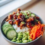 A close-up of a Sticky Teriyaki Chicken Poke Bowl Easy Dinner, featuring glazed chicken, rice, edamame, cucumber, and shredded carrots.