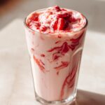 A tall glass filled with a creamy Strawberry Glaze Smoothie, swirled with vibrant red strawberry sauce and topped with fresh strawberries.