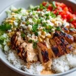 Close-up of a Street Corn Chicken Rice Bowl featuring sliced grilled chicken, rice, corn, lettuce, tomatoes, and a creamy sauce.