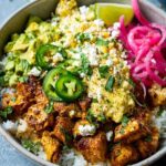 Close-up of a Street Corn Chicken Rice Bowl topped with seasoned chicken, corn, avocado, jalapenos, and pickled onions.