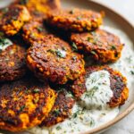 A close-up shot of crispy Sweet Potato Lentil Patties served on a plate with a creamy yogurt sauce and fresh dill.