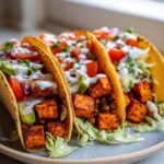 Three delicious Sweet Potato Lentil Tacos filled with roasted sweet potato cubes, lentils, avocado, tomatoes, and creamy sauce.
