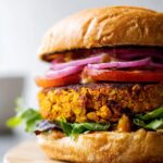 A delicious sweet potato red lentil veggie burger on a bun with lettuce, tomato, and red onion.
