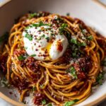 Close-up of a bowl of Tomato Garlic Pasta with Burrata, topped with fresh herbs and chili flakes.