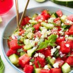 A close-up of a vibrant Watermelon Feta Cucumber Salad with fresh mint and red onion, garnished with basil leaves.