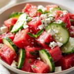 Close-up of a vibrant Watermelon Feta Mint Summer Salad in a bowl, featuring cubed watermelon, feta cheese, cucumber slices, and fresh mint leaves.