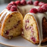 Close-up of a White Chocolate Raspberry Bundt Cake, sliced to reveal raspberries and white chocolate chips, topped with glaze and fresh raspberries.
