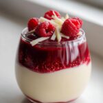 A close-up of White Chocolate Raspberry Mousse Cups Easy Dessert, layered with white chocolate mousse, raspberry sauce, and topped with fresh raspberries and white chocolate shavings.